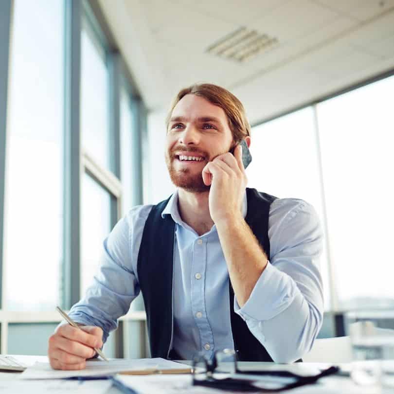 Mann im Büro telefoniert und notiert sich Informationen – symbolisiert eine persönliche & kostenlose Erstberatung für Hebammenversicherungen.